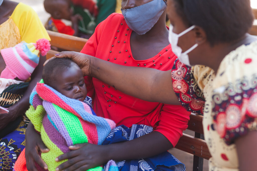 Nurse touching a baby's head while his mother holds him.